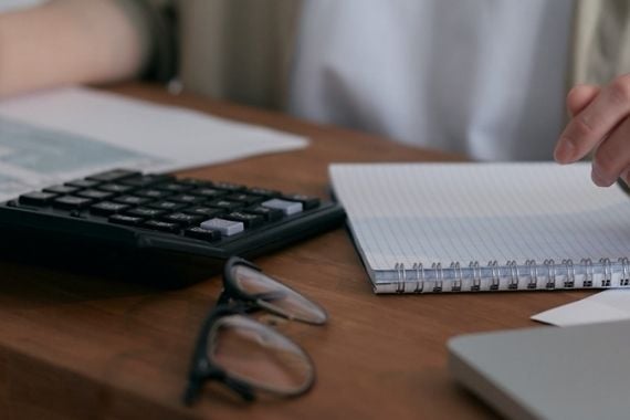 A desk with a keyboard, notepad and glasses on