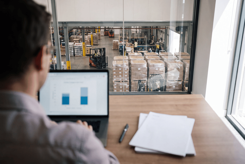 A manager reviewing cost figures at a desk overlooking the warehouse floor