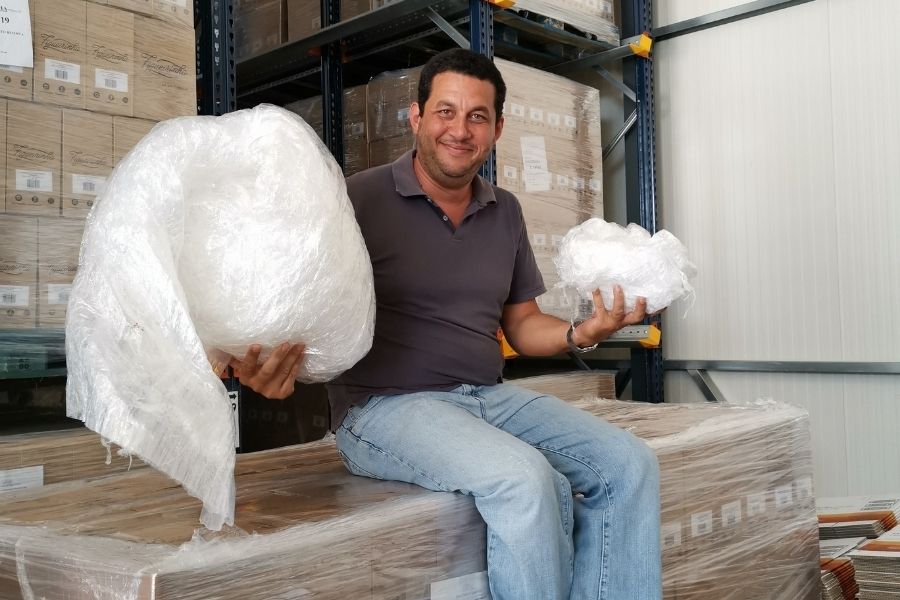 Member of Packaging Innovations holding up plastic sitting on boxes wrapped in plastic 